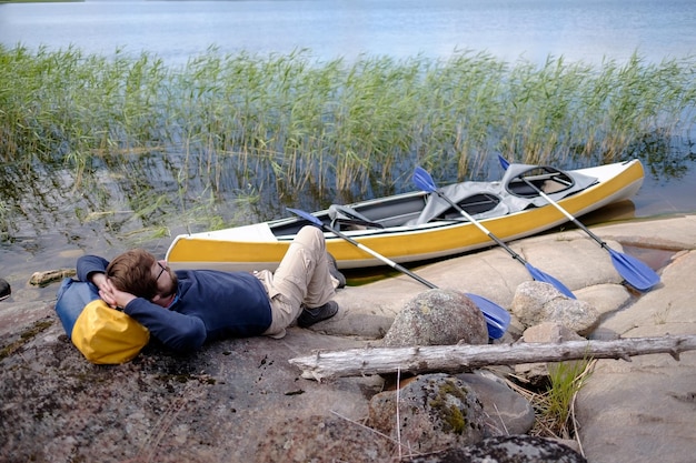 Homem descansando depois de viajar no caiaque fica na costa rochosa e desfruta de belas paisagens