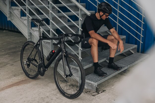 Homem descansando em uma escada de metal após andar de bicicleta ativa