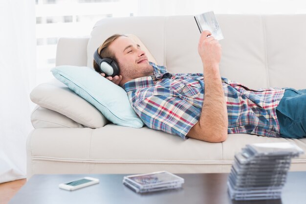 Homem descontraído, ouvindo música, deitado no sofá