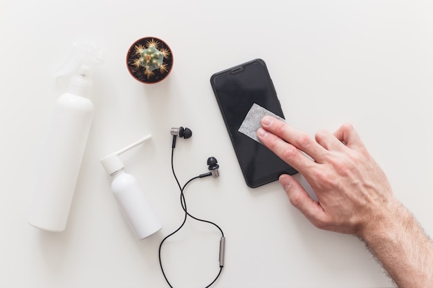 Homem desinfeta limpeza do smartphone com pano antibacteriano para prevenir o coronavírus COVID-19