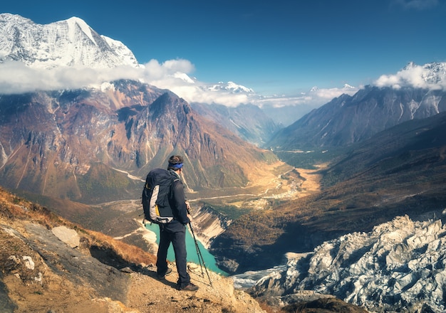 Homem desportivo em pé com mochila no pico da montanha e olhando no belo vale da montanha ao pôr do sol