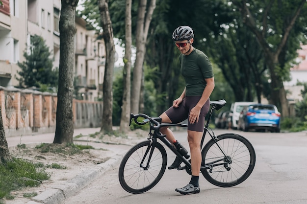 Homem desportivo parado com uma bicicleta preta na rua da cidade