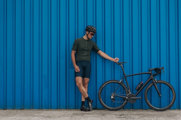 Homem desportivo posando perto de uma parede azul com uma bicicleta esportiva