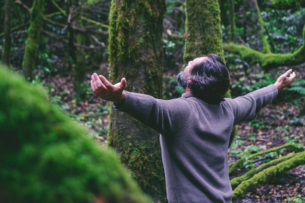 Foto homem despreocupado com os braços estendidos de pé na floresta relaxado e meditando felicidade e serenidade equilíbrio interior estilo de vida saudável natural árvores verdes e florestas fundo ao ar livre lazer