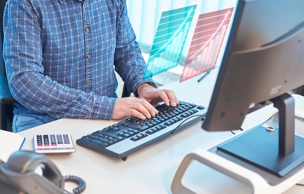 Homem digitando em um computador em uma mesa de escritório, exibição de relatórios 3d de produção flutuante