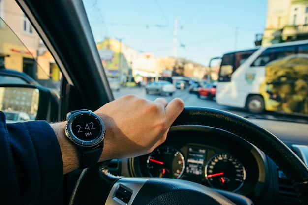 Homem dirigindo carro no trânsito da cidade olhando no relógio em primeira pessoa tarde para reunião