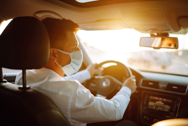 Homem dirigindo um carro coloca uma máscara médica durante uma epidemia na cidade de quarentena.