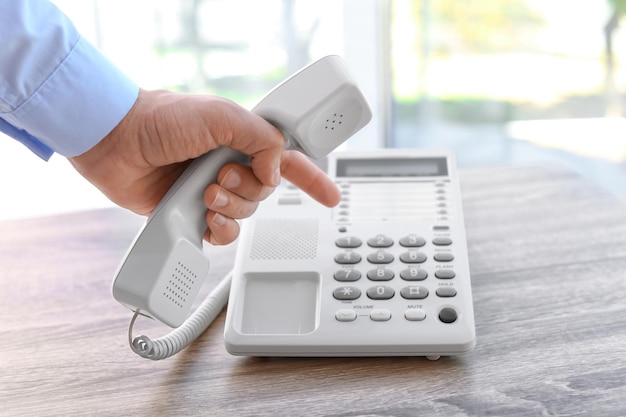 Homem discando número no telefone na mesa dentro de casa