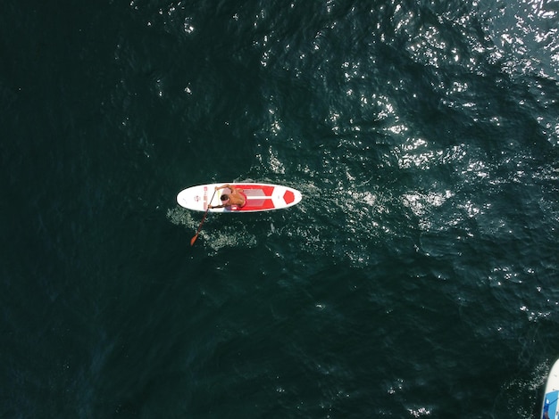 Homem do mar sup vista de cima para baixo no homem atleta nadando no mar e paddleboarding ao pôr do sol de verão saudável