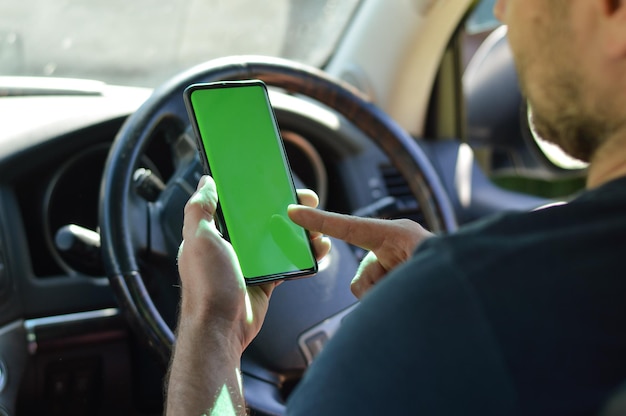 homem do ombro que está sentado no carro com volante à direita e segura o celular na mão Tela verde