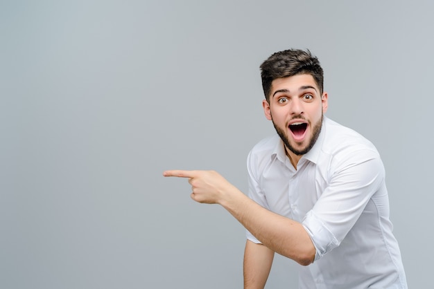 Homem do Oriente Médio atraente aponta para copyspace isolado sobre fundo cinza