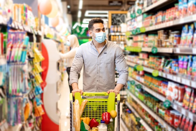 Homem do Oriente Médio fazendo compras usando máscara comprando comida no supermercado