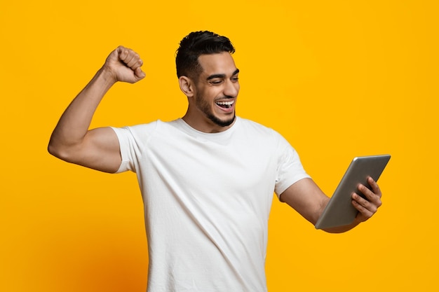 Homem do Oriente Médio positivo negociando on-line usando pad desfrutando de sucesso