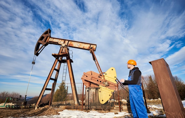 Homem do petróleo verificando o trabalho do jack da bomba do poço de petróleo