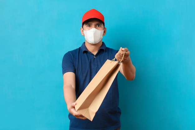 Foto homem do serviço de entrega usando máscara facial com uniforme azul segura um saco de papel com espaço para cópia