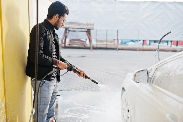 Homem do sul da ásia ou homem indiano lavando seu transporte branco na lavagem de carros.