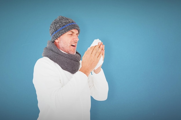 Homem doente na moda de inverno espirrando contra o fundo azul