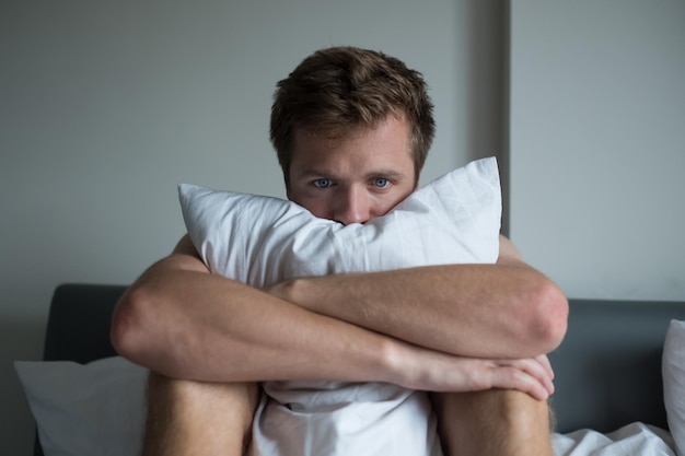 Foto homem doente sentado em sua cama com a cabeça na mão