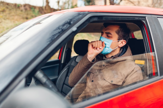 Homem doente, sentado no carro, usando máscara protetora, tossindo com coronavírus da gripe. Proibição de dirigir com febre.