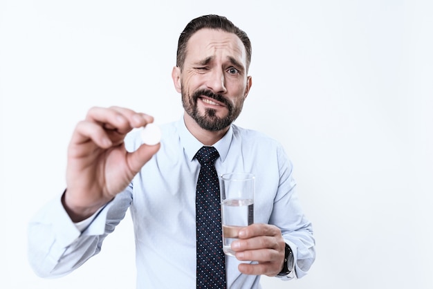 Foto homem doente tem um comprimido e um copo de água nas mãos.