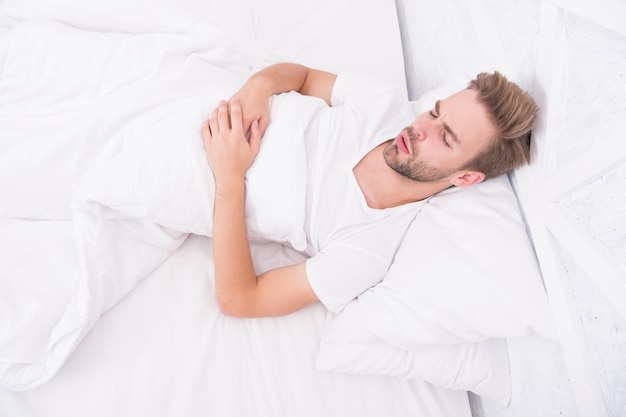 Homem dorme na cama de manhã cedo homem dormindo quarto branco aconchegante fim de semana em casa tempo para relaxar cara adormecer conceito de saúde masculina tendo um sonho Conceito de paz