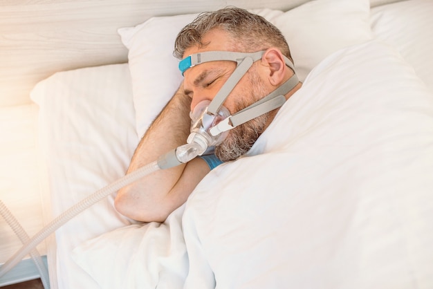 Foto homem dormindo com problemas respiratórios crônicos usando máquina de cpap na cama