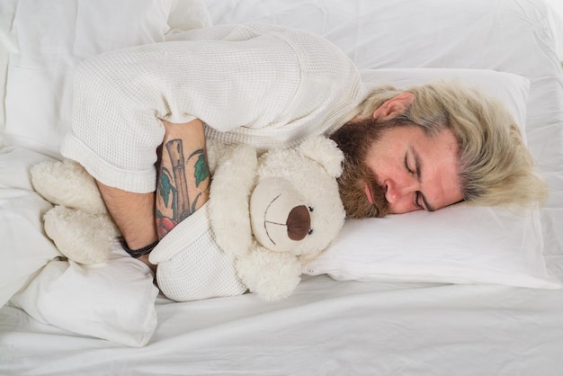 Homem dormindo na cama homem barbudo na cama de manhã e acordando homem dormindo com ursinho de pelúcia ursinho de pelúcia