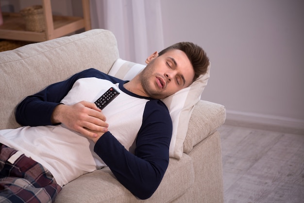 Homem dormindo no sofá com controle remoto de tv em suas mãos.