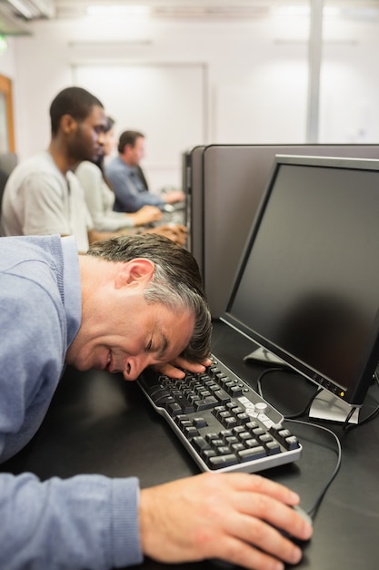 Homem dormindo no teclado na classe de computador