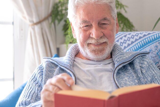 Homem dos anos 70 sentado no sofá, lazer e conceito de pessoas, homem sênior barbudo feliz relaxando em casa lendo livro