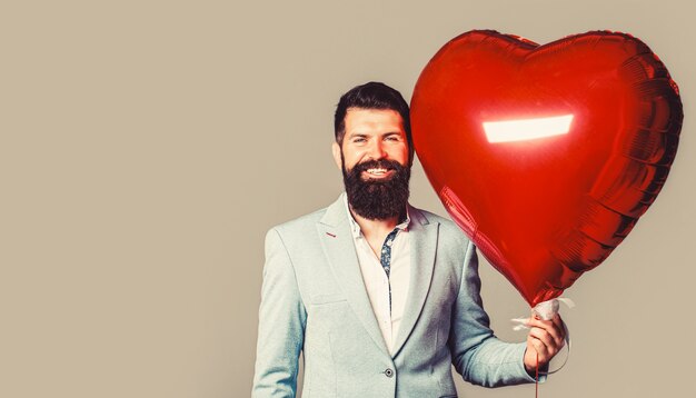 Homem dos namorados com balão de ar vermelho. homem feliz com balões de ar em forma de coração. dia dos namorados. coração vermelho. corações de amor.