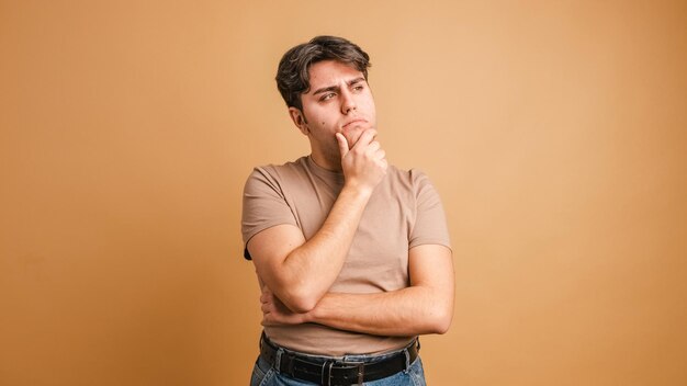 Foto homem duvidoso de pé com a mão no queixo com expressão pensativa