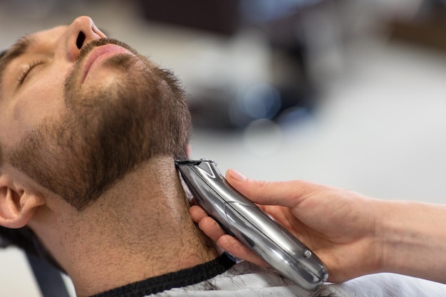 Foto homem e barbeiro com cortador cortando barba no salão