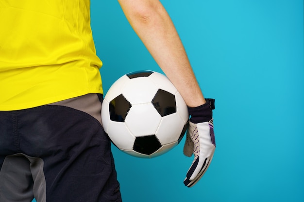 Homem é fã de futebol com camiseta amarela e bola de futebol no fundo azul