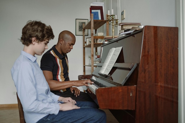 Homem e menino adolescente sentados ao lado do piano Foto de estoque