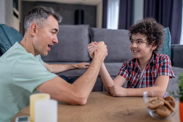 Foto homem e menino sentados à mesa lutando nas mãos