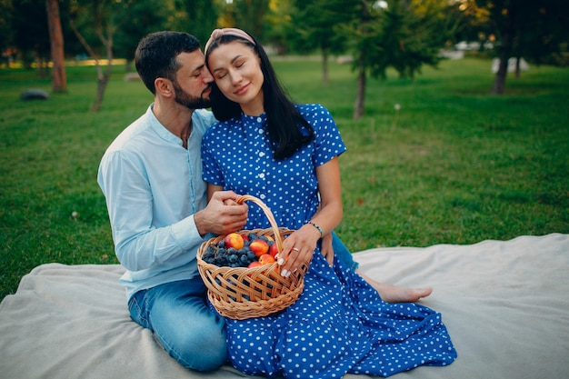 Homem e mulher adulta jovem casal piquenique sentado com cesta de frutas no prado de grama verde no parque.