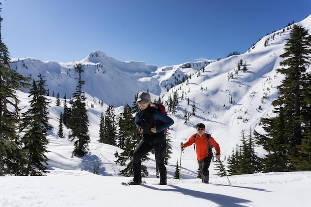 Homem e mulher aventureiros estão andando com raquetes de neve na neve