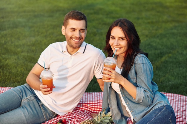 Homem e mulher bebendo smoothies de frutas frescas no piquenique no parque