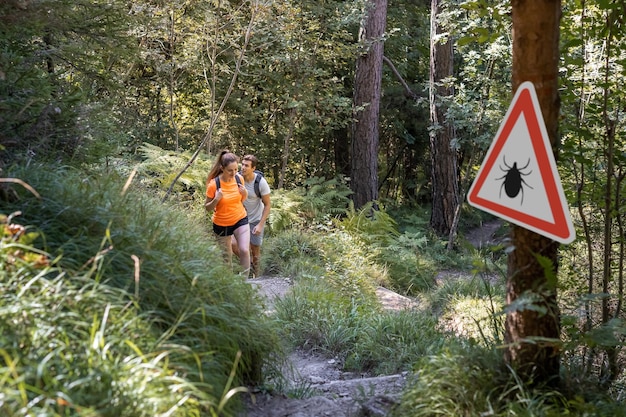 Homem e mulher caminhando na floresta de carrapatos infectados com sinal de alerta Risco de doença transmitida por carrapatos e Lyme