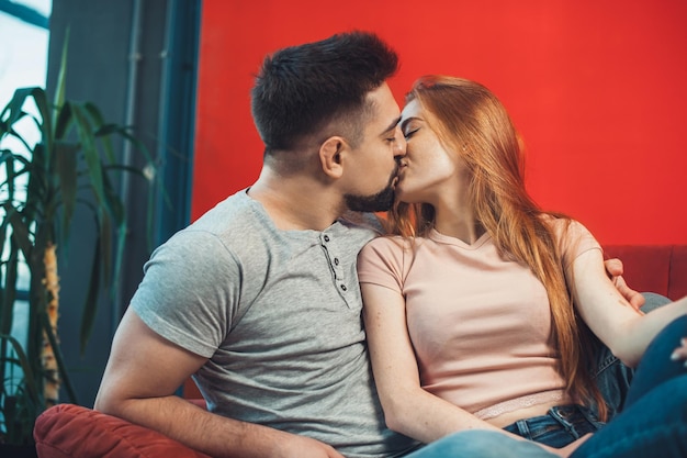 Homem e mulher caucasianos se beijando e se abraçando enquanto estão sentados no sofá, passando o fim de semana juntos ...