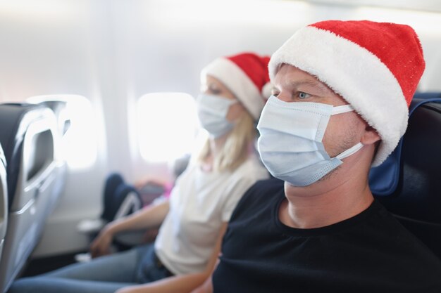 Homem e mulher com chapéu de Papai Noel e máscaras protetoras voando no avião. Jornada de ano novo durante o covid 19 conceito de pandemia