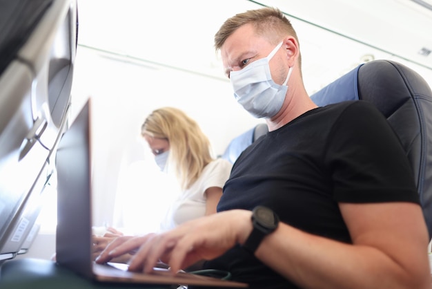 Homem e mulher com máscaras protetoras, trabalhando em laptops na cabine da aeronave