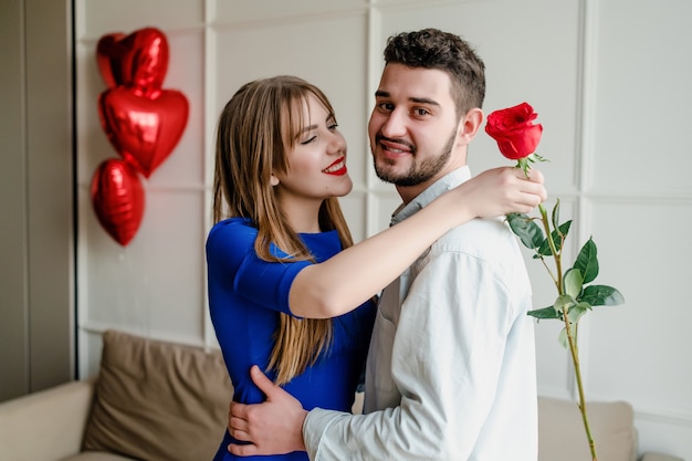 Homem e mulher com rosa vermelha em casa com balões em forma de coração