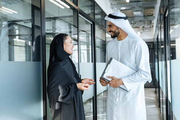 Homem e mulher com roupas tradicionais dos Emirados trabalhando em um escritório de negócios de Dubai
