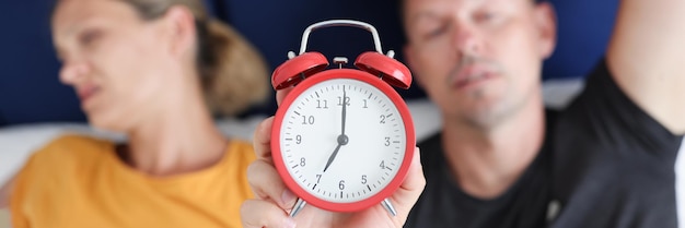 Homem e mulher com sono, deitados na cama, segurando o despertador vermelho closeup conceito de despertar precoce