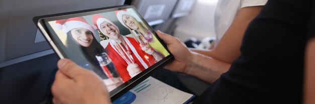 Homem e mulher comemorando o Natal com amigos em chapéus de Papai Noel através da tela da mesa digital ...