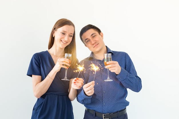 Homem e mulher comemorando o Natal ou a festa de véspera de ano novo com luzes de Bengala e taças de champanhe no fundo branco.