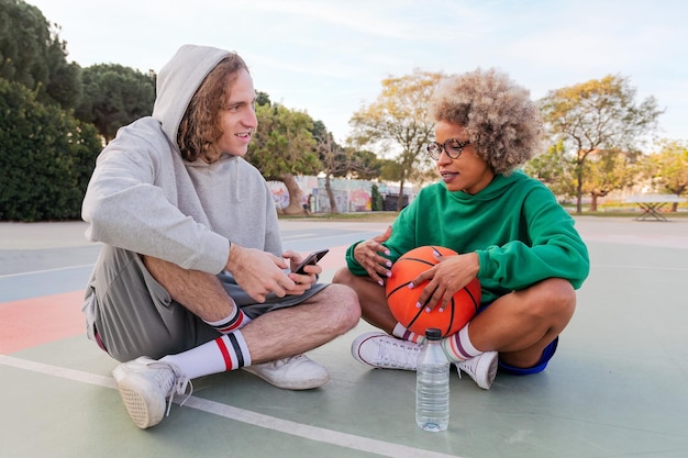 Homem e mulher conversam e se divertem sentados na quadra depois de jogar basquete em um parque da cidade conceito de amizade e esporte urbano na rua