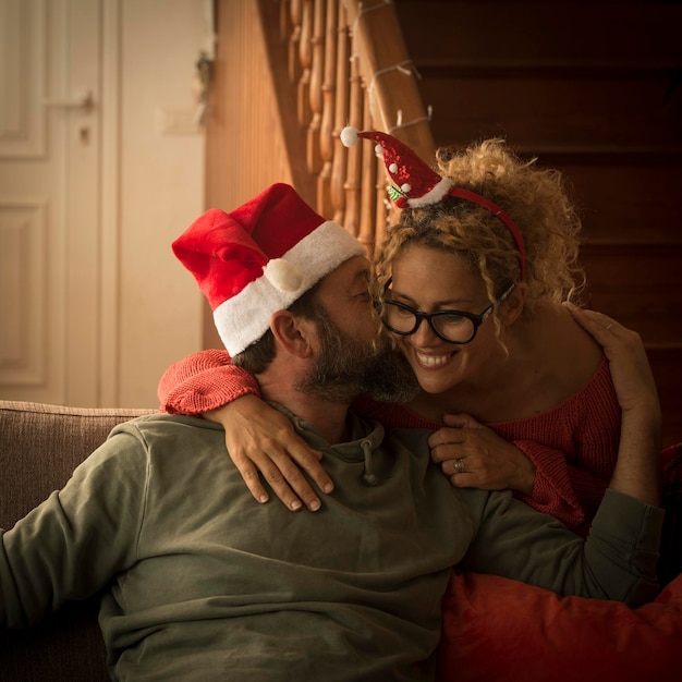 Homem e mulher em casa usando chapéu de papai noel beijando com amor e romance Casal feliz em relacionamento aproveita a temporada de férias de natal Mulher abraçando homem e apartamento no fundo Ano novo
